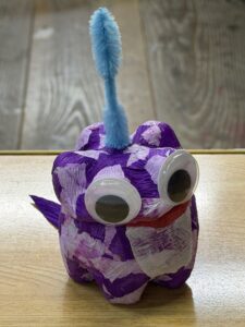 紫色の紙を貼り、大きめの目玉シールと天辺に青いモールを飾りつけたペットボトルランタン作品