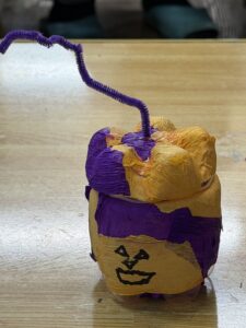 紫とオレンジのクレープペーパーを貼り、帽子と紫の蝶ネクタイをつけたペットボトルランタン作品