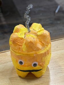 黄色とオレンジの紙を貼り、目玉シールと黒い大きな口をつけたカボチャ風のペットボトルランタン作品