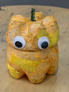 黄色とオレンジの紙を貼り、大きめの目玉シールと緑のモールを飾ったペットボトルランタン作品