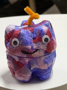 紫やピンクのクレープペーパーを貼り、目玉シールと橙色のモールで飾られたペットボトルランタン作品