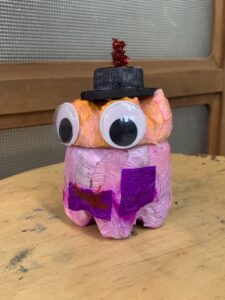 ピンクやオレンジの紙を貼り、大きな目玉と黒いシルクハット、紫の蝶ネクタイをつけたペットボトルランタン作品