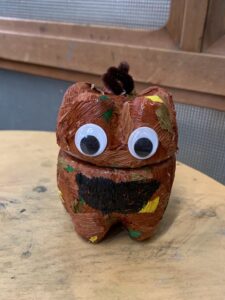 茶色とオレンジの紙を貼り、大きな目玉シールと大きな黒い口をつけたカボチャ風のペットボトルランタン作品