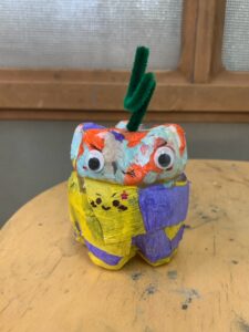 黄色と青のクレープペーパーを貼り、大きめの目玉シールと緑のモールをつけたペットボトルランタン作品