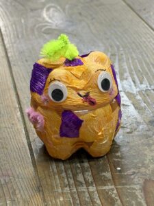 黄色の紙をベースに紫色と緑の装飾を施し、目玉シールと天辺に緑のモールをつけたペットボトルランタン作品